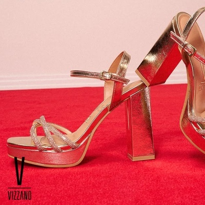 Sandálias douradas com salto alto largo e tiras brilhantes em tapete vermelho
