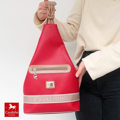 Mochila vermelha com detalhes bege e logótipo Cavalinho segurada por uma pessoa.