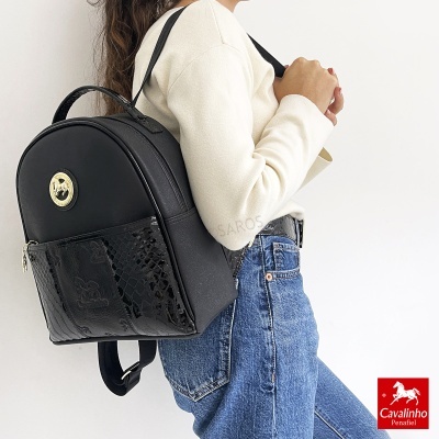 Mochila preta com fecho dourado e textura imitação cobra usada por pessoa com jeans e camisola creme