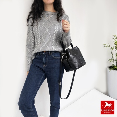 Mulher com camisola cinza e jeans azul segurando mala de mão preta com padrão em relevo