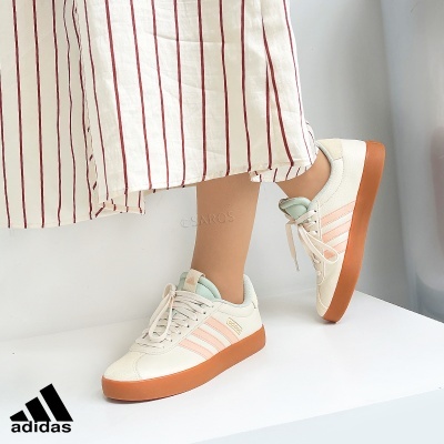 Ténis Adidas creme e cor-de-rosa com sola castanha junto a saia branca às riscas vermelhas.