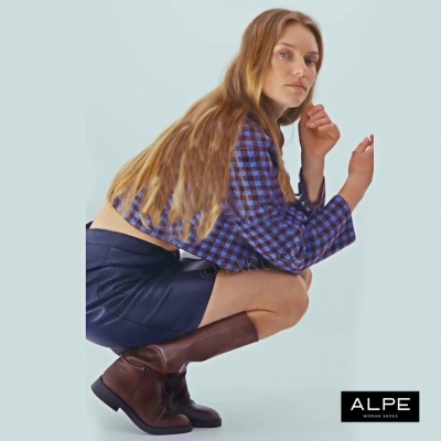 Mulher com casaco xadrez azul e preto, saia preta e botas marrons de couro