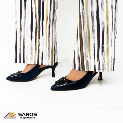 Sapatos pretos de salto médio com fivela e calças de riscas verticais.