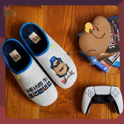 Chinelos cinzentos com interior azul, texto e personagem, comando de videojogo e jogos em chão de madeira