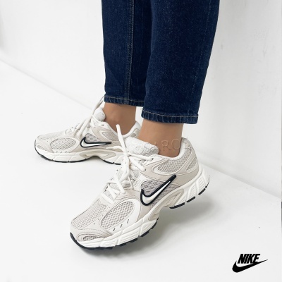 Ténis Nike brancos com logo preto usados com calças jeans escuras