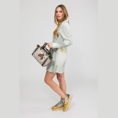 Mulher com vestido claro e mala decorada segura mala de mão cinzenta e usa sapatilhas coloridas.