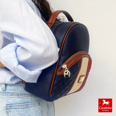 Mochila de várias cores da Cavalinho usada por pessoa com camisa branca e jeans claros