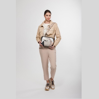 Mulher com mala pequena prateada e preta vestindo roupa bege clara em fundo branco.