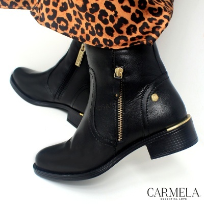 Botins pretos em pele com fecho dourado lateral e salto baixo, usados com calças de padrão animal print.