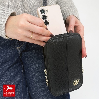 Carteira preta em pele com fecho dourado e logótipo CV dourado, mãos femininas a colocar telemóvel rosa