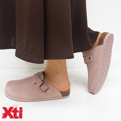 Sapatos mule cor-de-rosa claro com fivela e sola texturada, usados com calças castanho escuras.