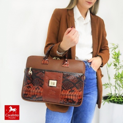 Mala castanha com padrão serpente e detalhes dourados, com mulher vestindo casaco castanho