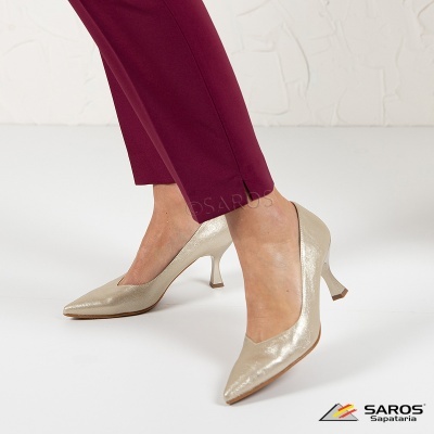 Sapatos de salto médio dourados com calças vinho num fundo branco.