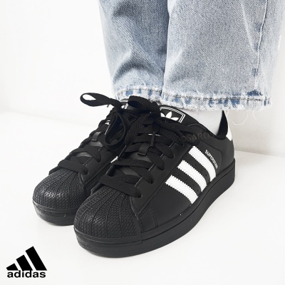 Ténis Adidas Superstar pretos com riscas brancas usados com calças de ganga claras