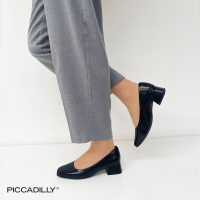 Sapatos de salto baixo pretos em verniz com bico quadrado e calças cinzentas.