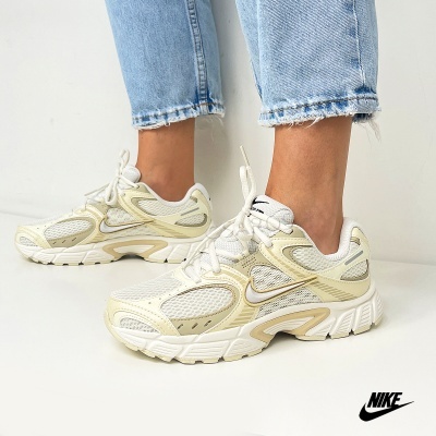 Sapatos desportivos Nike brancos e bege com sola branca e atacadores brancos, usados com calças de ganga claras.