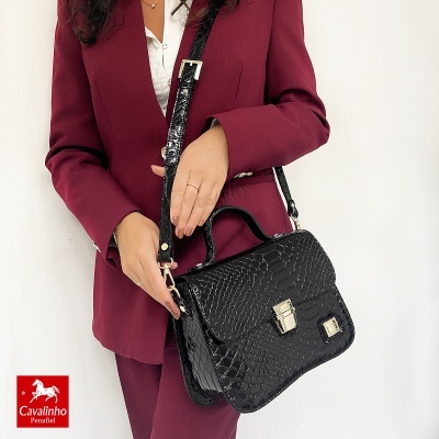 Mulher com fato vinho e mala preta croco com fecho metálico