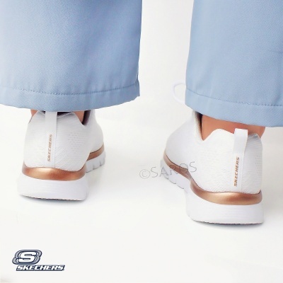 Ténis brancos Skechers com detalhes em cobre vistos de costas com calças azuis claras.
