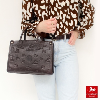 Mala de mão castanha com padrão Cavalinho em pele, usada com camisa castanha padrão branco e jeans claros.
