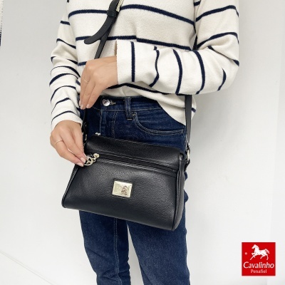 Mala preta de pele com fecho metálico usada por pessoa com camisola às riscas e calças de ganga.