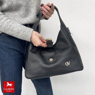 Mala preta de couro granulada com fecho dourado e logótipo CV, segurada por mulher com camisola cinzenta e jeans azuis