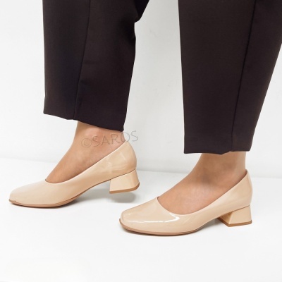 Sapatos bege verniz de salto baixo quadrado com calças pretas sobre fundo branco