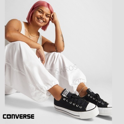 Pessoa sentada a usar ténis Converse pretos com sola branca em fundo branco