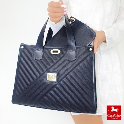 Mala de mão preta matelassê com alças, segurada por pessoa com roupa branca