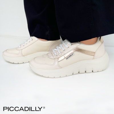 Ténis femininos creme com detalhes dourados e sola branca da Piccadilly, usados com calças escuras.