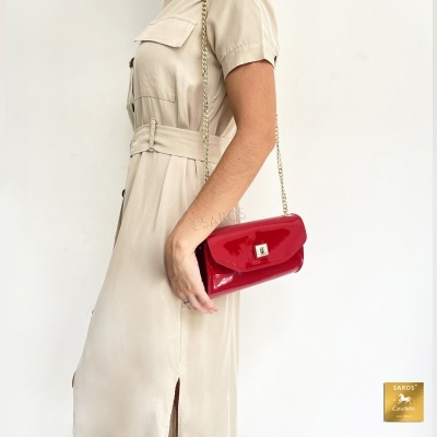 Mala vermelha de verniz com alça de corrente dourada, usada com vestido bege claro.
