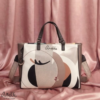 Mala tote multicolor com padrão abstrato e alças castanhas sobre tecido rosa