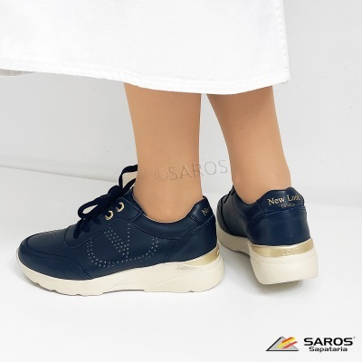 Ténis pretos com sola branca e detalhes dourados usados com vestido branco