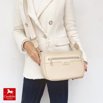 Carteira bege claro com alça larga, usada por pessoa com casaco creme e jeans escuros