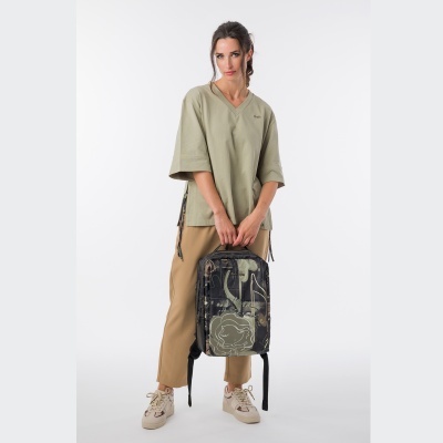 Mulher com camisola verde clara, calças bege e mochila preta camuflada