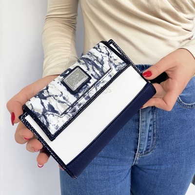 Carteira feminina azul e branca com padrão mármore segurada por pessoa com camisola creme e calças de ganga