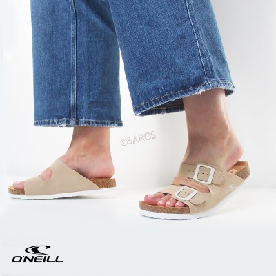 Sandálias castanhas claras com sola branca e de cortiça, uma com duas fivelas, outra com tira larga, vistas em fundo branco.