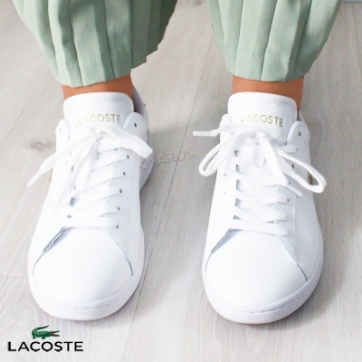 Ténis brancos Lacoste com logótipo dourado na língua e atacadores brancos