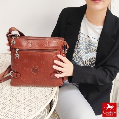 Mala castanha em pele Cavalinho com padrão gravado numa mesa branca com pessoa vestida de blazer preto