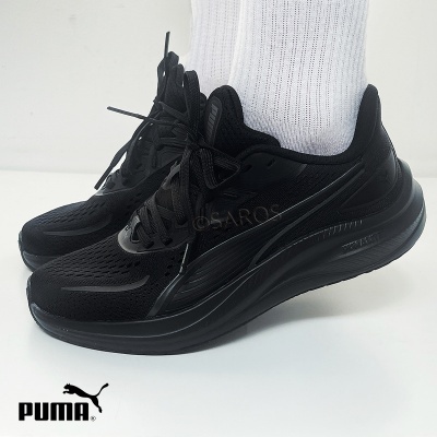 Par de sapatilhas pretas Puma com atacadores, usadas com meias brancas sobre fundo branco.