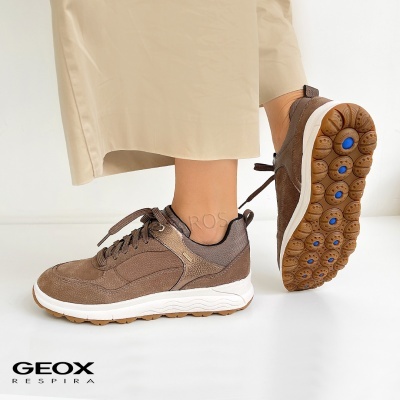 Ténis castanhos Geox com sola branca e detalhes azuis, calça bege, fundo branco