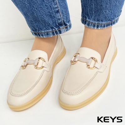 Sapatos mocassins creme com detalhe dourado e solado bege claro, usados com calças de ganga azuis