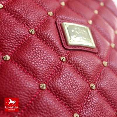 Mala de couro vermelho matelassê com tachas douradas e placa metálica com a marca Cavalinho Penafiel