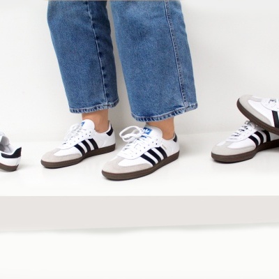 Sapatilhas Adidas brancas com riscas pretas e sola castanha em fundo branco