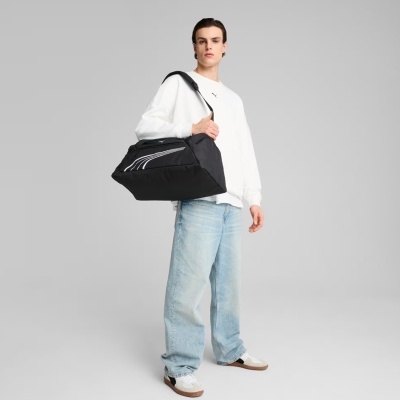 Homem com sweatshirt branca, jeans azuis largos e mala preta com listras brancas