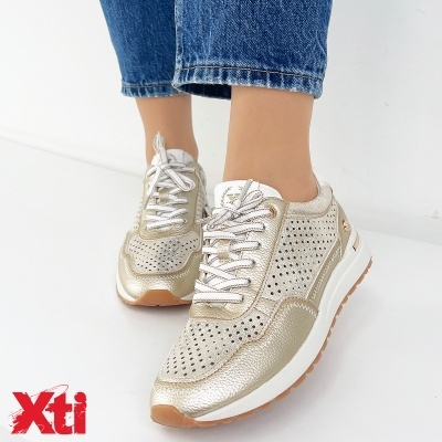 Ténis dourados Xti com perfurações e sola branca em fundo branco