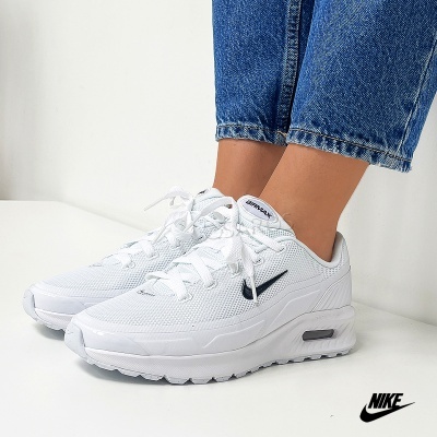 Ténis Nike Air Max brancos com logótipo preto usados com calças de ganga azuis