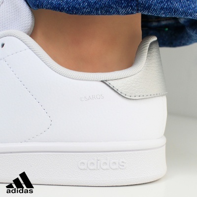 Ténis Adidas branco com detalhe cinza e texto SAROS em relevo no calcanhar.