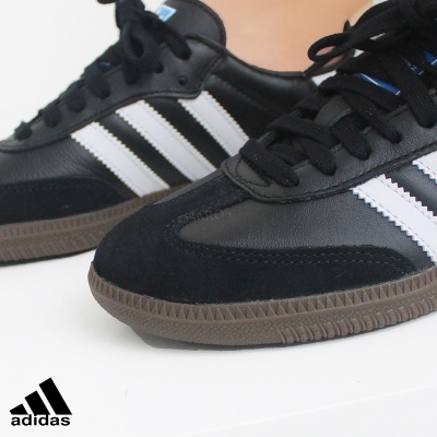 Ténis Adidas preto com riscas brancas e sola castanha em fundo branco