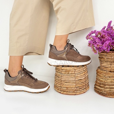 Ténis castanhos com sola branca e castanha usados por modelo, próximo a recipiente de vime com flores lilases.