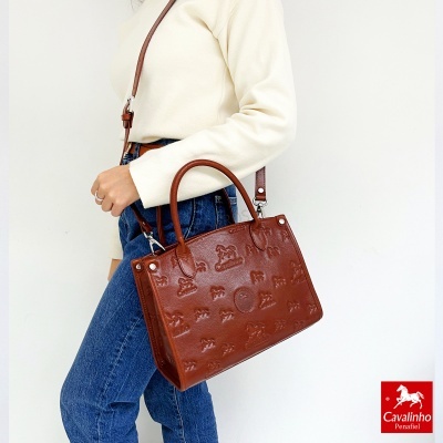 Bolsa castanha em pele com padrão em relevo e alça, usada por mulher